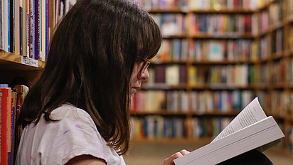 Eine junge Frau in einer Bibliothek liest in einem Fachbuch