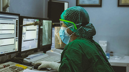 Eine Frau in medizinischer Schutzkleidung bedient einen Computer in einem Krankenhaus.