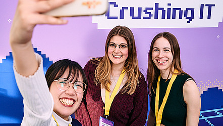 Drei Studierende machen ein Selfie vor einer Pressewand: Tech Crush – Crushing IT