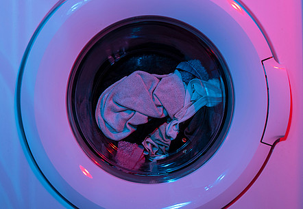 Eine Waschmaschine in buntem Licht, gerade dreht sich Wäsche in der Trommel