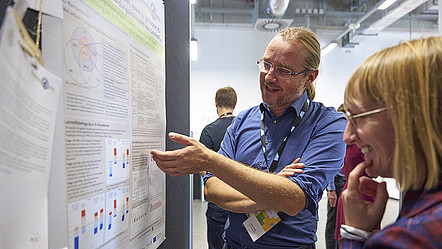 Zwei Personen diskutieren anhand eines Posters mit verschiedenen Graphen über informatische Inhalte