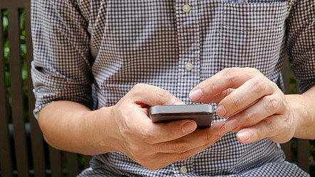Eine Person in kariertem Hemd scrollt auf ihrem Smartphone.