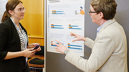 Zwei Frauen im Gespräch vor einem Poster zum Thema Bildungsverlauf von Frauen in der Informatik in Deutschland