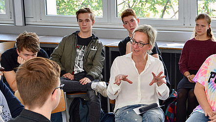 GI-Präsidentin Christine Regitz sitzt in einem Klassenzimmer mit Jugendlichen zusammen, unterhält sich mit ihnen und gestikuliert dabei mit den Händen
