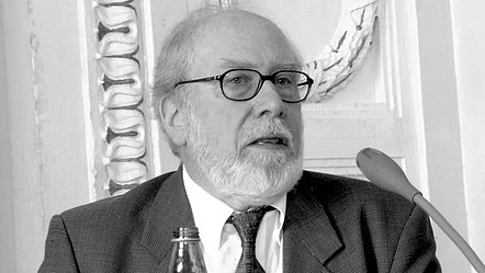 Niklaus Wirth auf einem Panel mit Mikrofon und Wasserflasche. Das Bild ist schwarz-weiß.