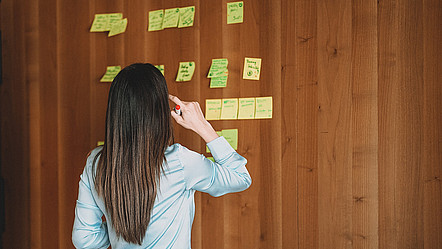 Eine Frau steht vor einer Wand, an der mehrere Post-it-Notizen angeheftet wurden
