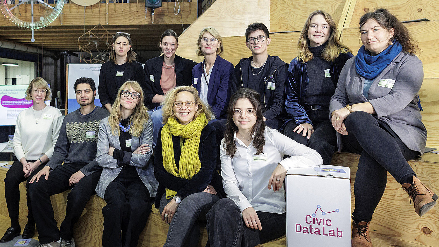 Das Team des Civic Data Lab sitzt auf einer Holzbühne