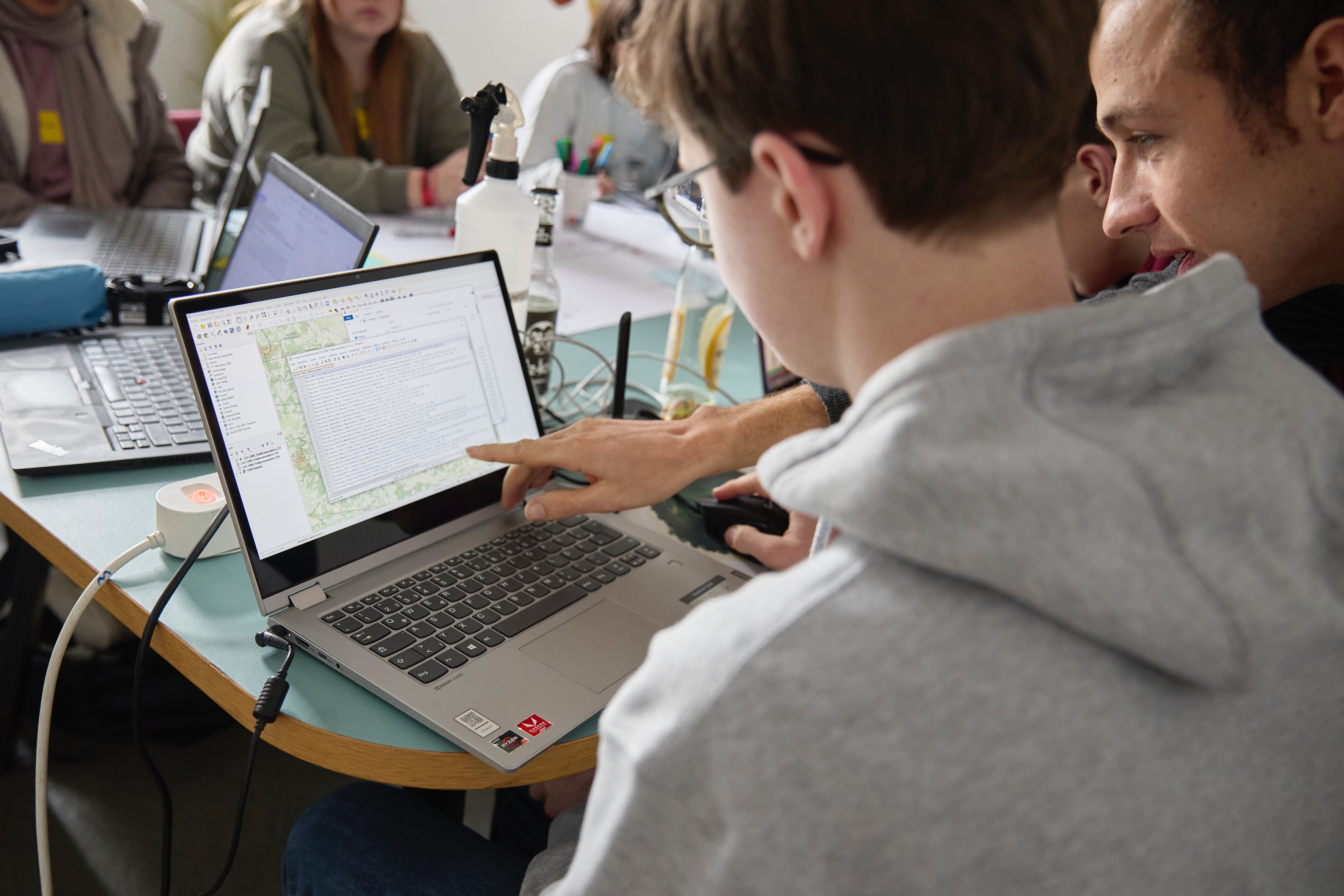 Ein jugendliches Kind sitzt am Laptop und bekommt etwas von einem erwachsenen Mann am Laptop gezeigt